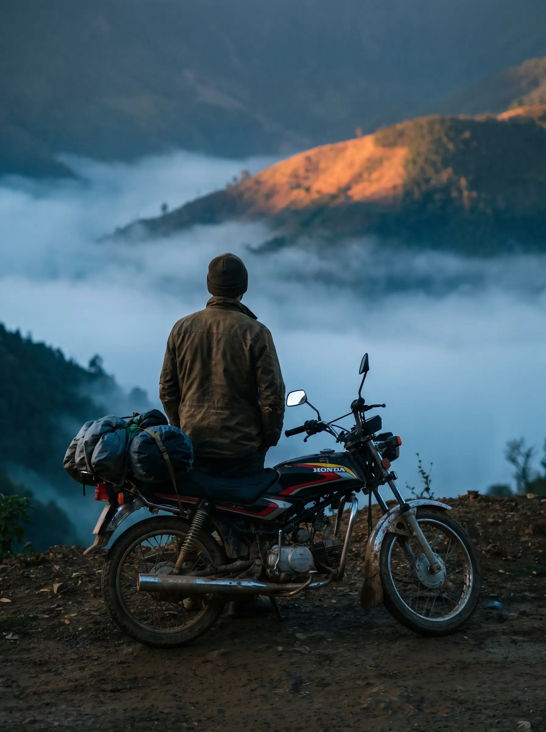 Rider standing beside a loaded motorcycle above a valley filled with bright morning mist