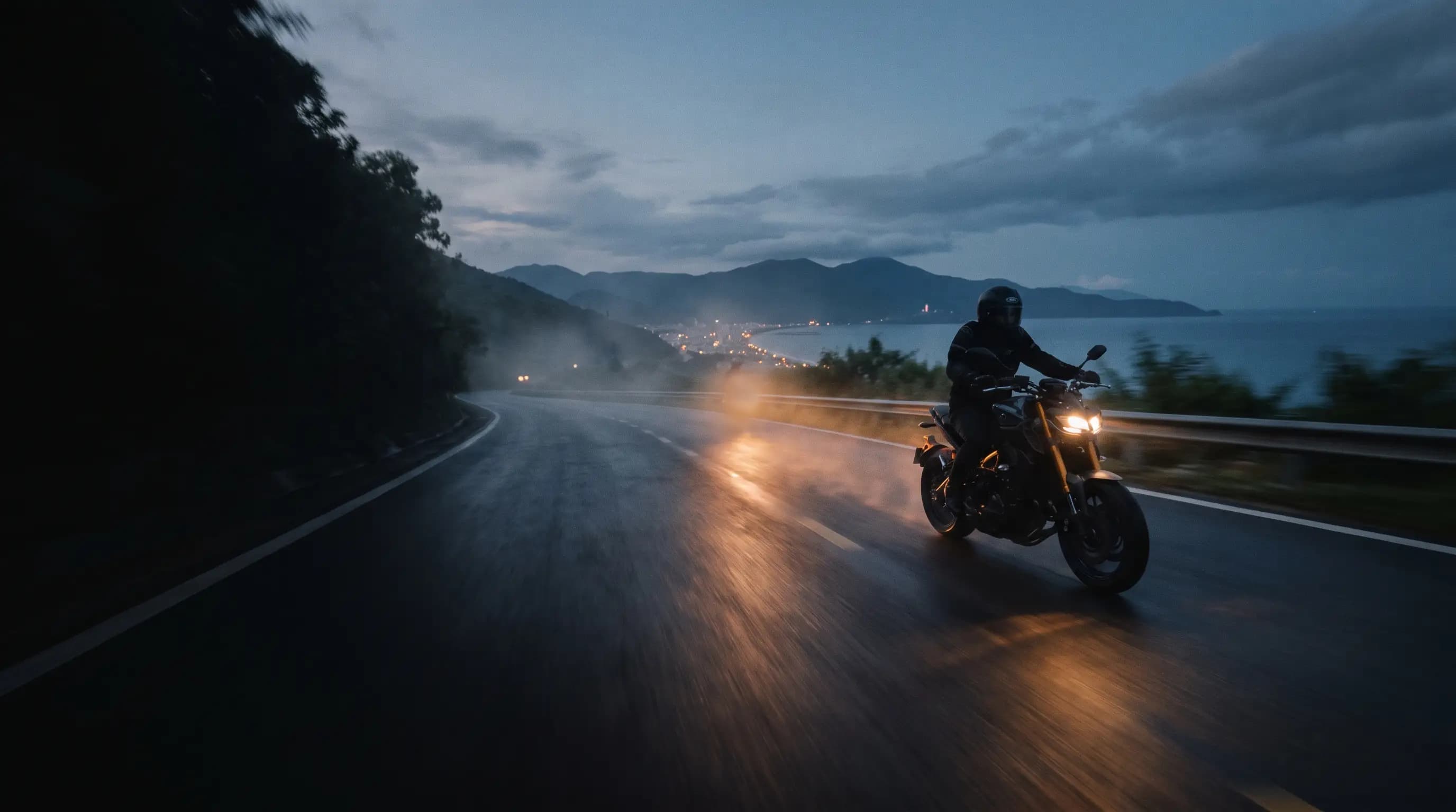 Motorcycle rider on a coastal mountain road above Da Nang at golden hour, low sun over the sea