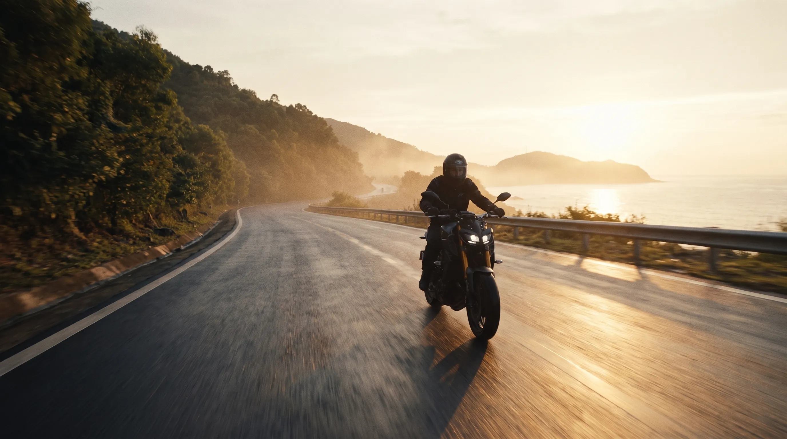 Motorcycle rider on a coastal mountain road above Da Nang at golden hour, low sun over the sea