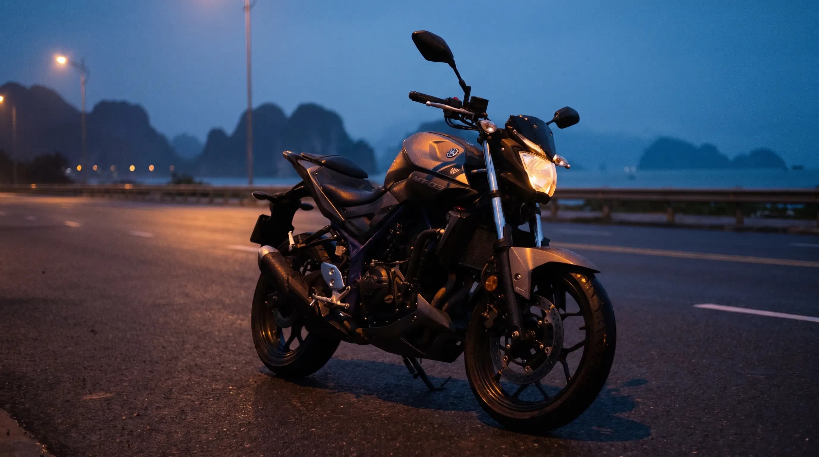 Yamaha MT-03 parked on a coastal road at blue hour with karst mountains behind