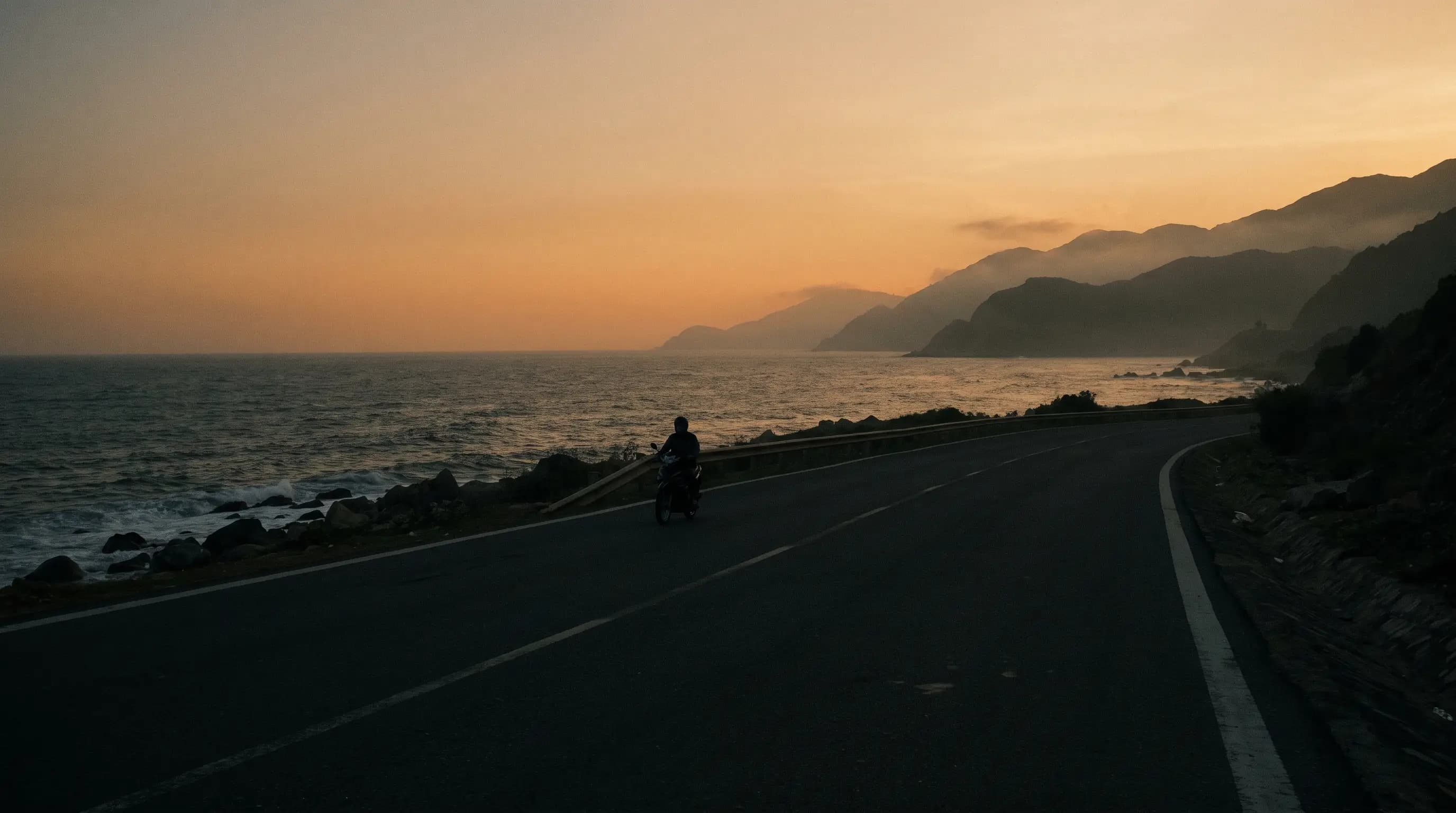 Lone rider on an empty coastal highway against a wide evening sky
